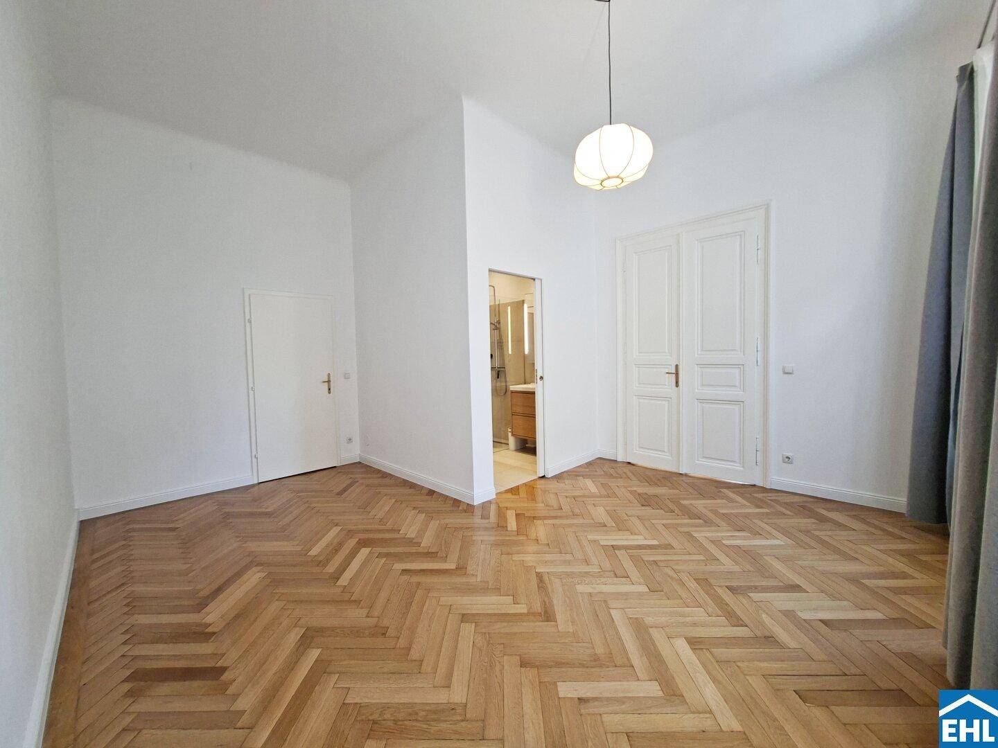 Schlafzimmer mit Fischgrätparkett, hohen Decken und Zugang zu einem angrenzenden Badezimmer.