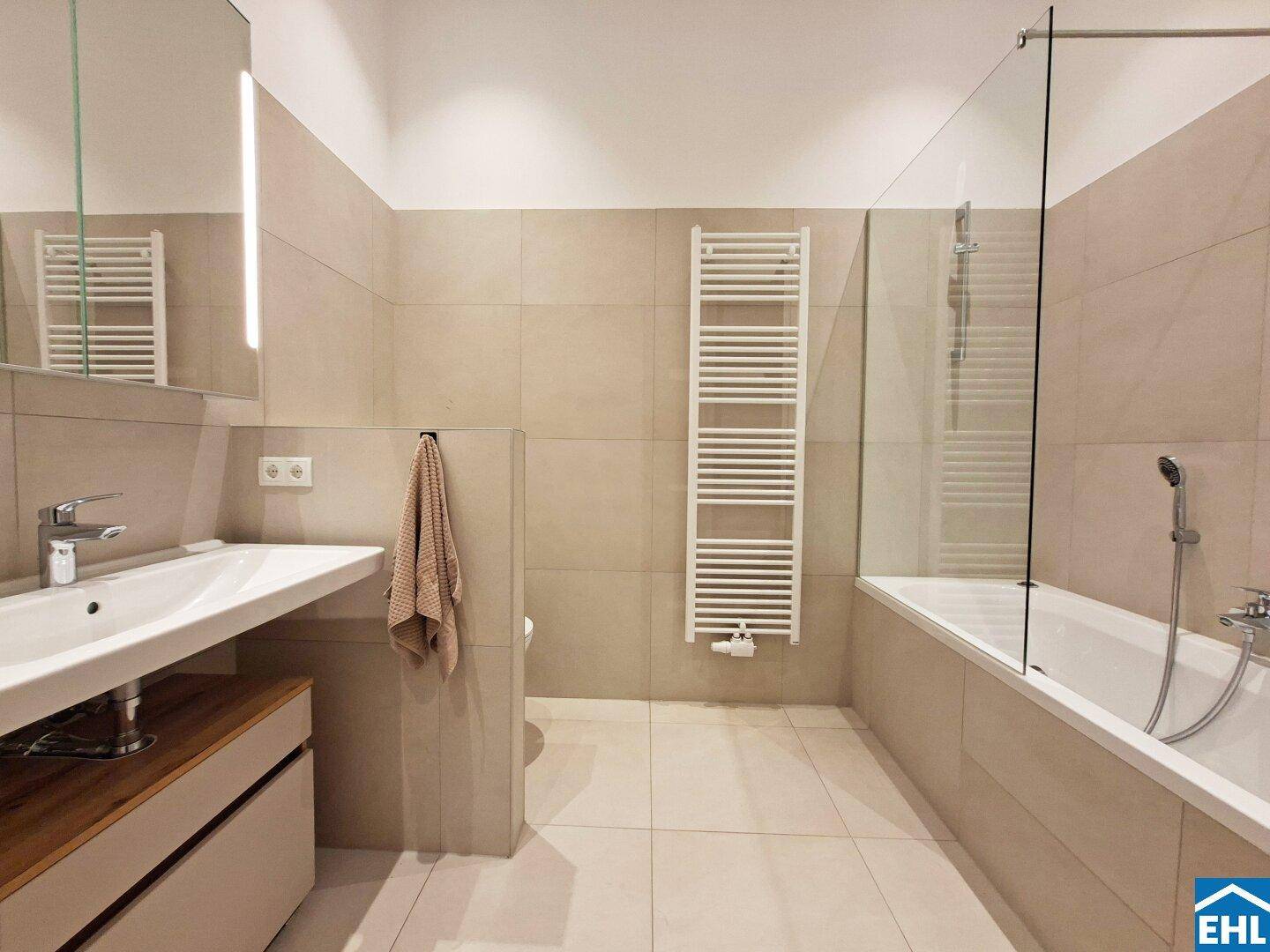 Modernes Badezimmer mit Badewanne, Einzelwaschbecken und beheiztem Handtuchhalter.