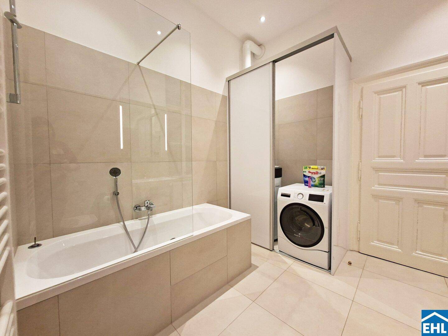 Badezimmer mit Badewanne, Duschabtrennung und integrierter Waschmaschine.