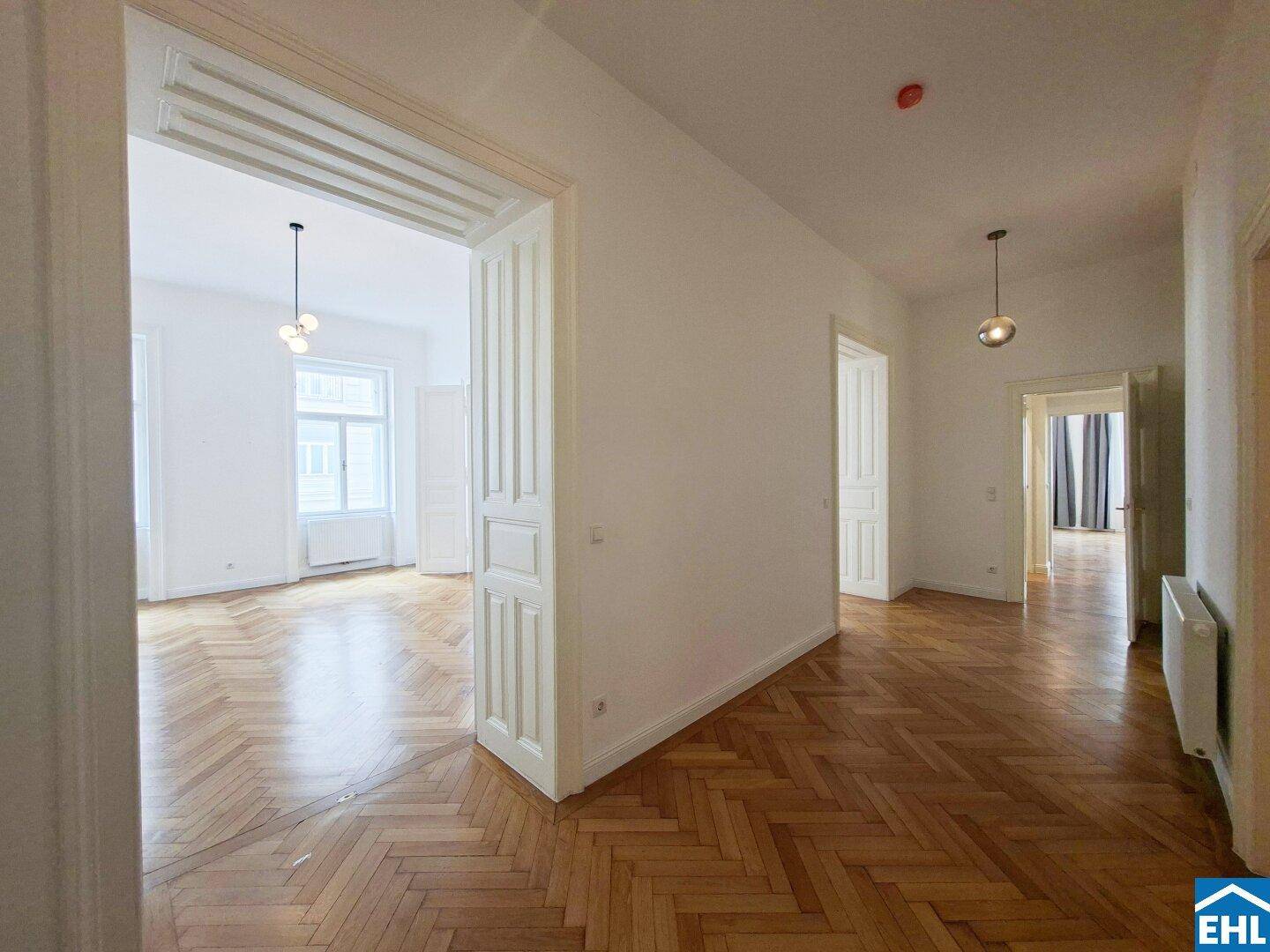 Geräumiger Flur mit Fischgrätparkett, hohen Decken und Blick in angrenzende Zimmer.
