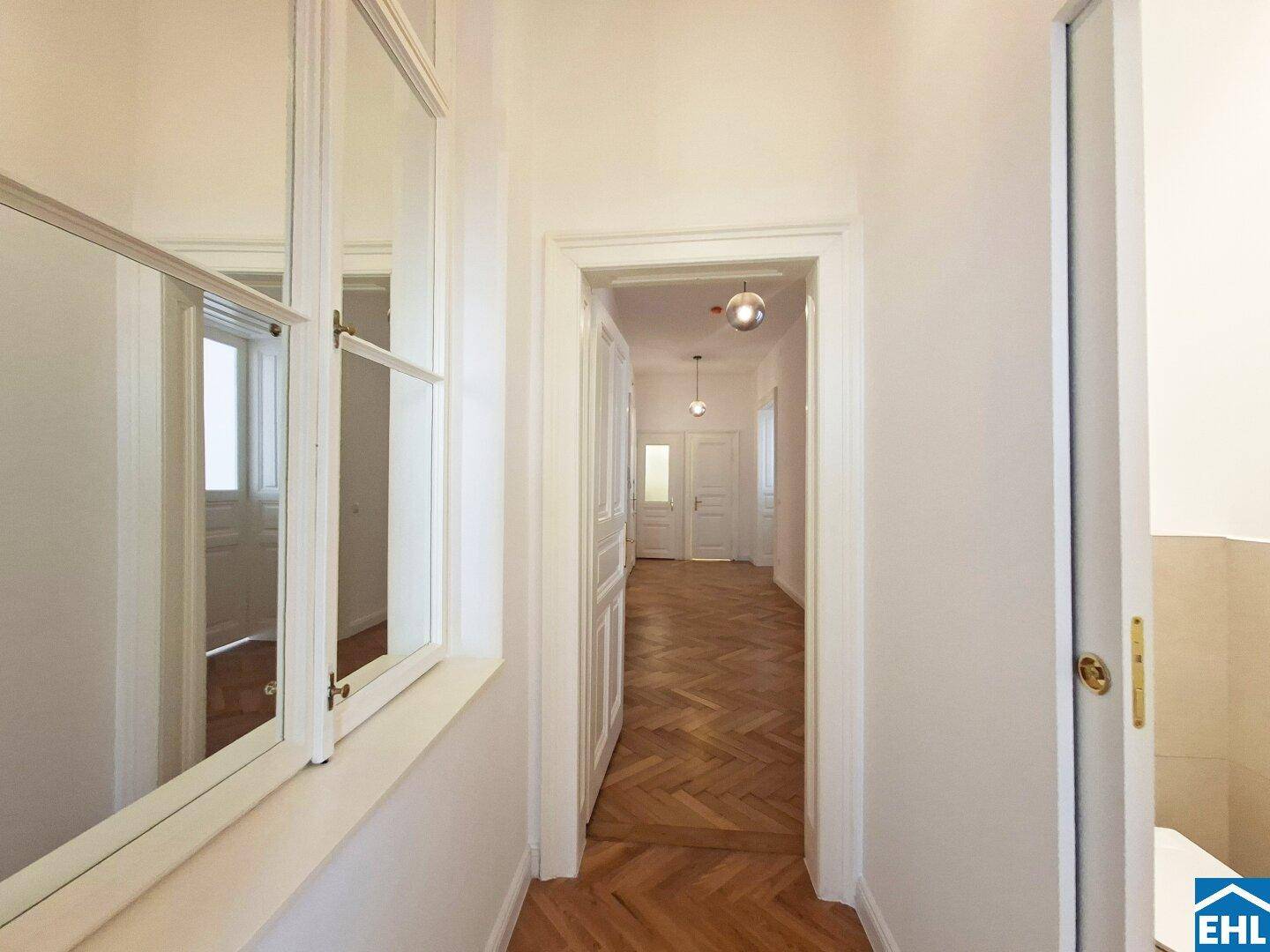 Flur mit Fischgrätparkett, hohen Decken und einem Fenster mit Blick in den Gang.