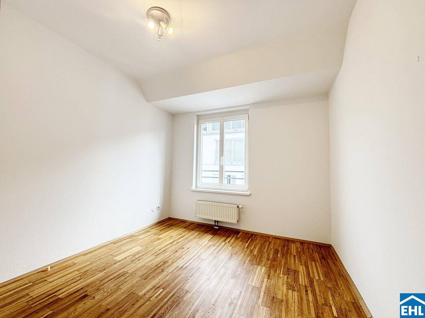 Gemütliches Schlafzimmer mit Holzboden und großem Fenster, das viel Tageslicht hereinlässt.