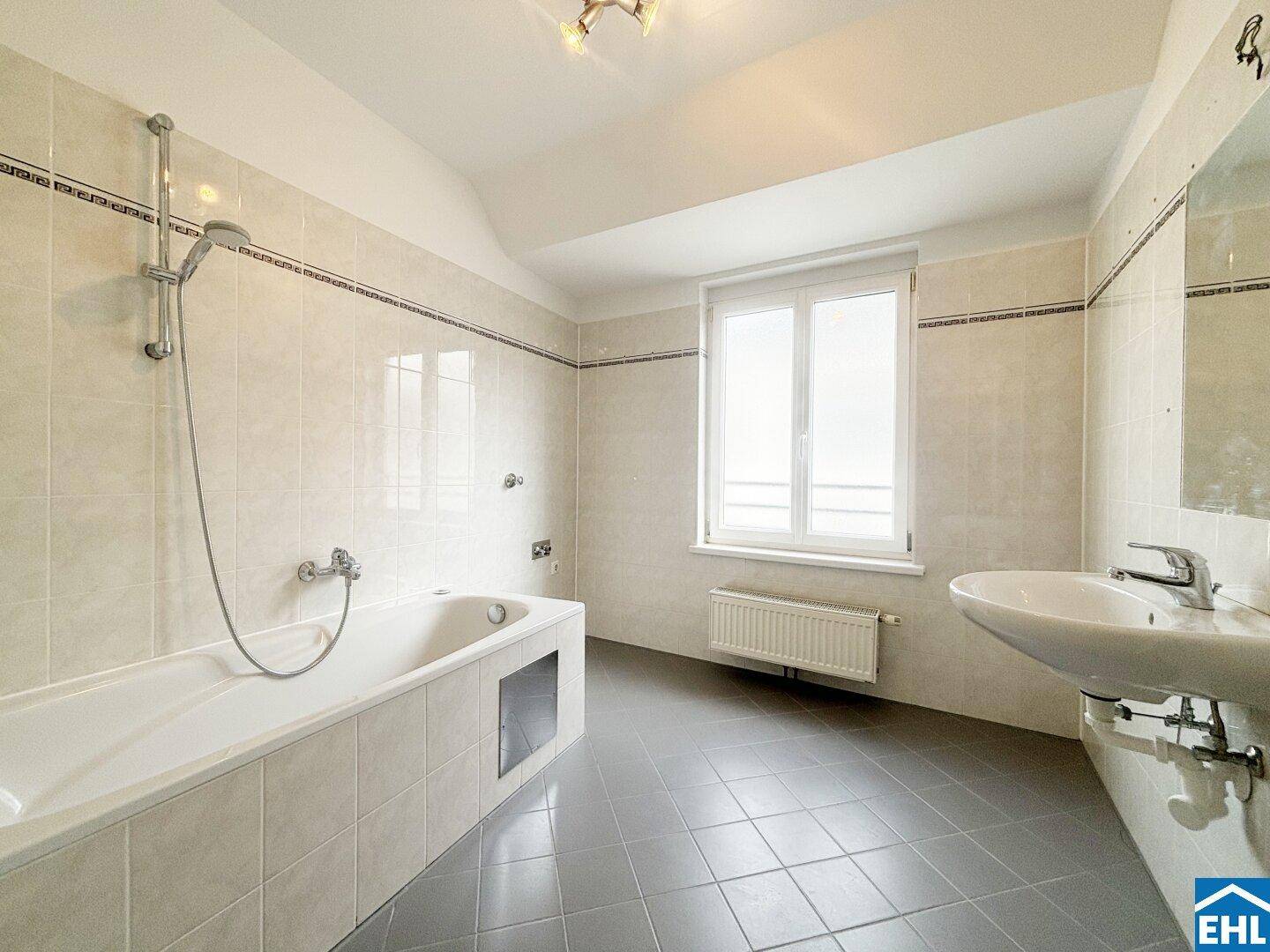 Geräumiges Badezimmer mit Badewanne, Waschbecken, Fliesen und Fenster für Tageslicht.