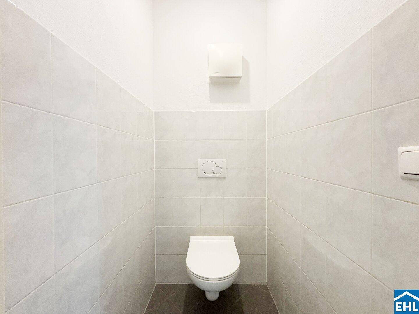 Modern gefliestes separates WC mit wandhängender Toilette und Lüftung.