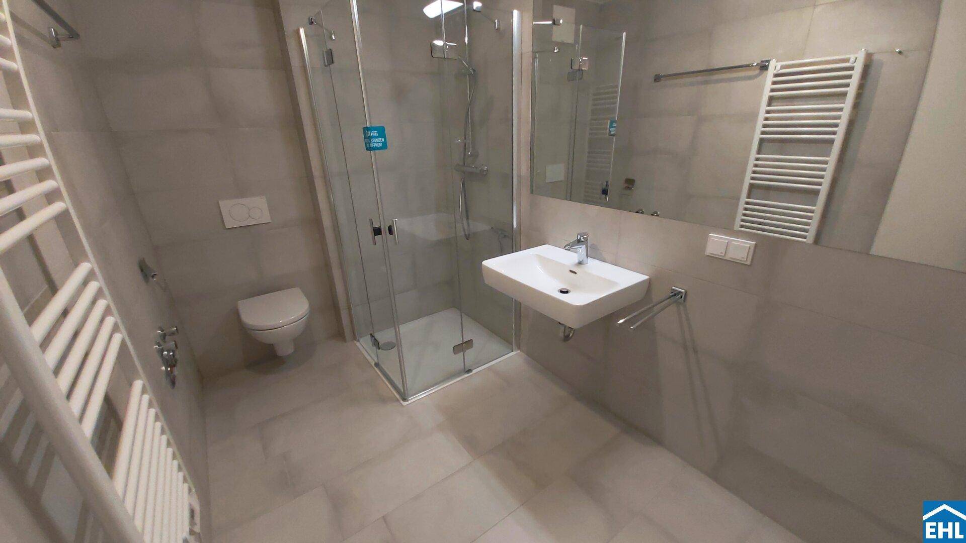 Modernes Badezimmer mit grauen Fliesen, Duschkabine, WC und beheiztem Handtuchhalter.