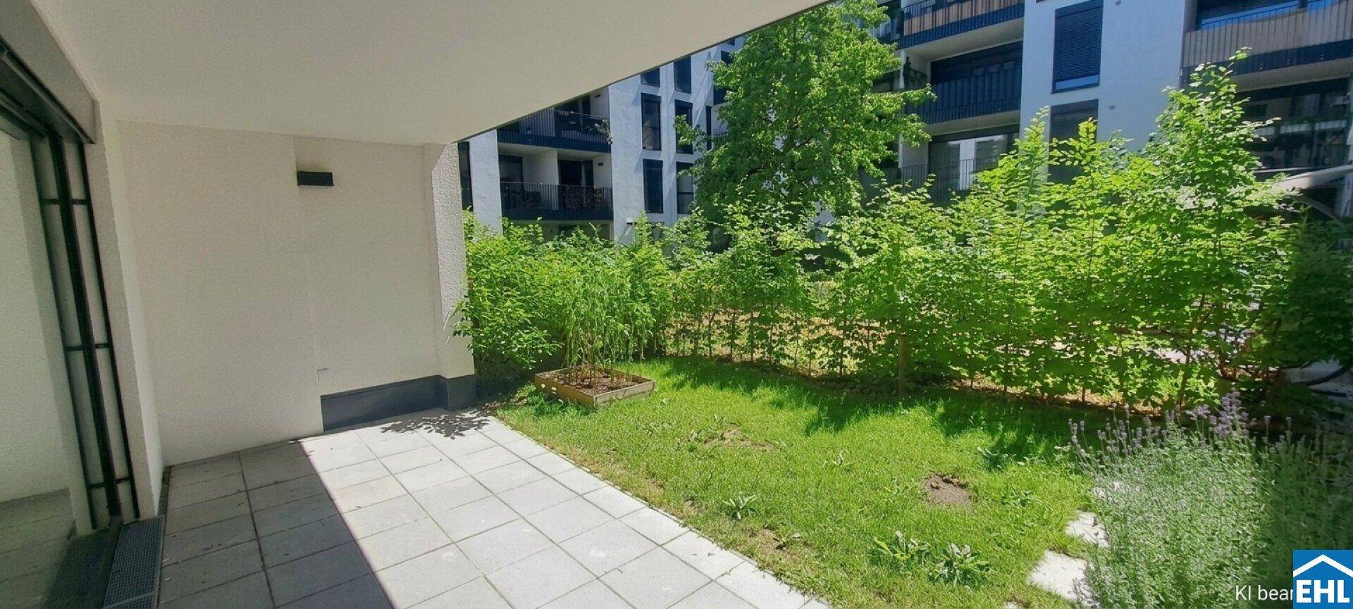 Gepflasterte Terrasse mit angrenzender Rasenfläche und grüner Hecke in einer modernen Wohnanlage.