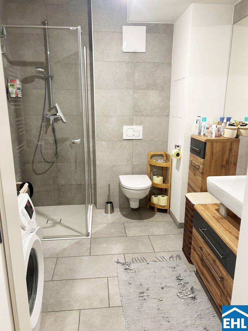 Modernes Badezimmer mit ebenerdiger Dusche, WC und Waschbecken, ausgestattet mit grauen Fliesen.