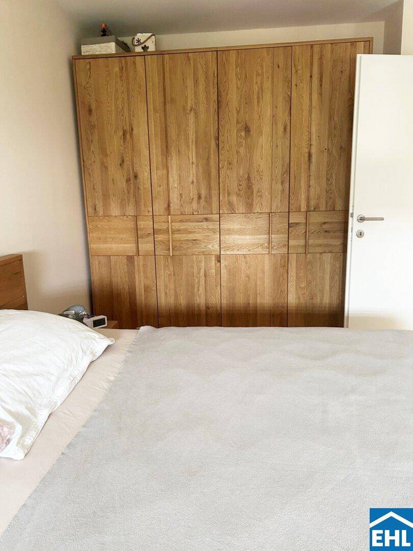 Schlafzimmer mit einem großen, modernen Kleiderschrank aus Holz und einem bequemen Bett.