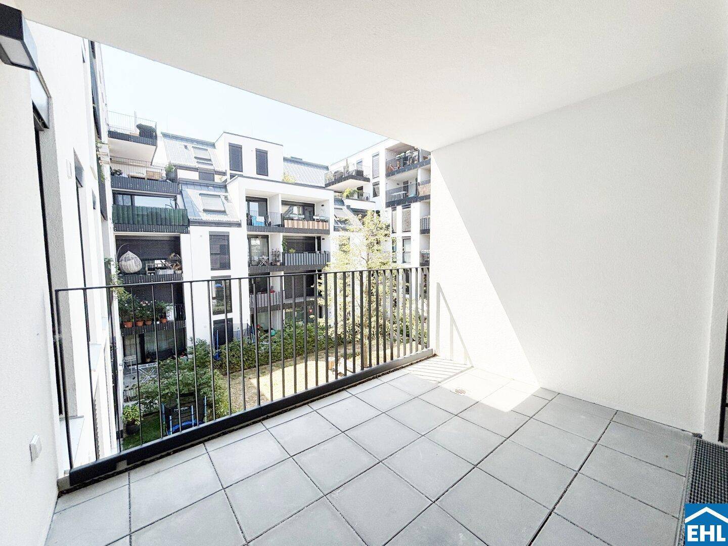 Heller Balkon mit Fliesenboden und Blick auf den begrünten Innenhof der Wohnanlage.
