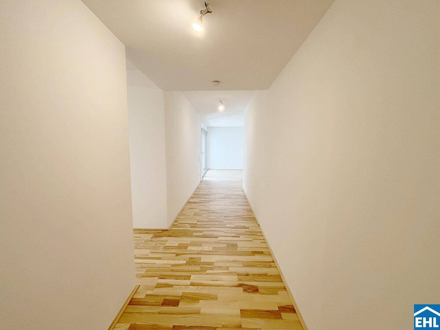 Langer, heller Flur mit Holzboden und weißen Wänden, der zu weiteren Räumen führt.