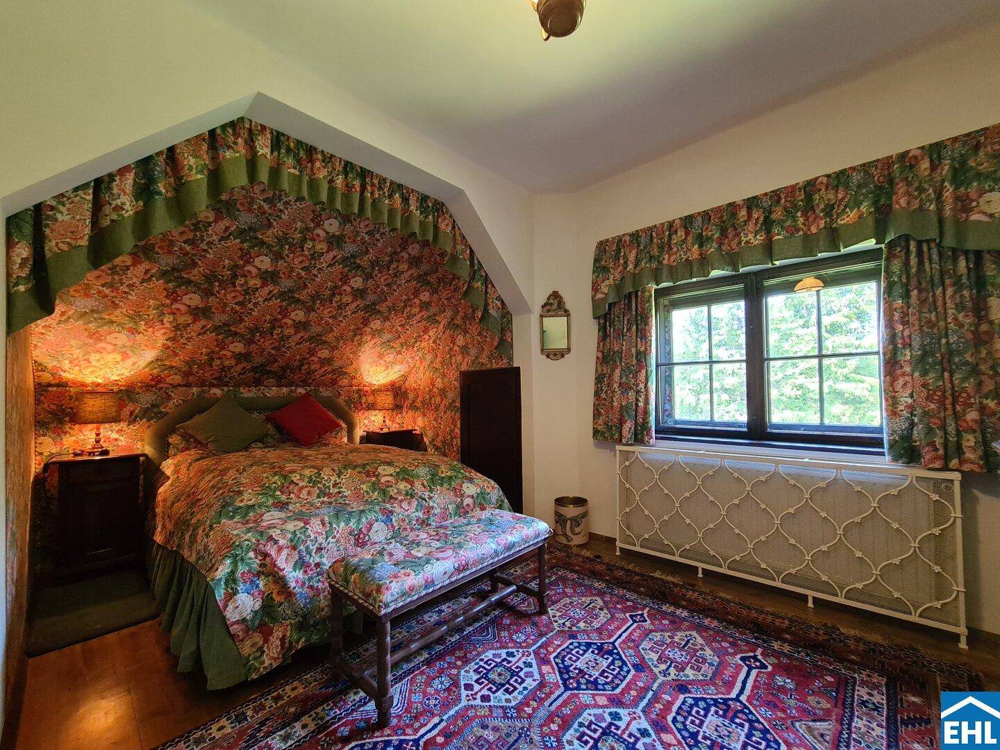 Gemütliches Schlafzimmer mit floraler Tapete, traditionellen Möbeln und Teppichboden.