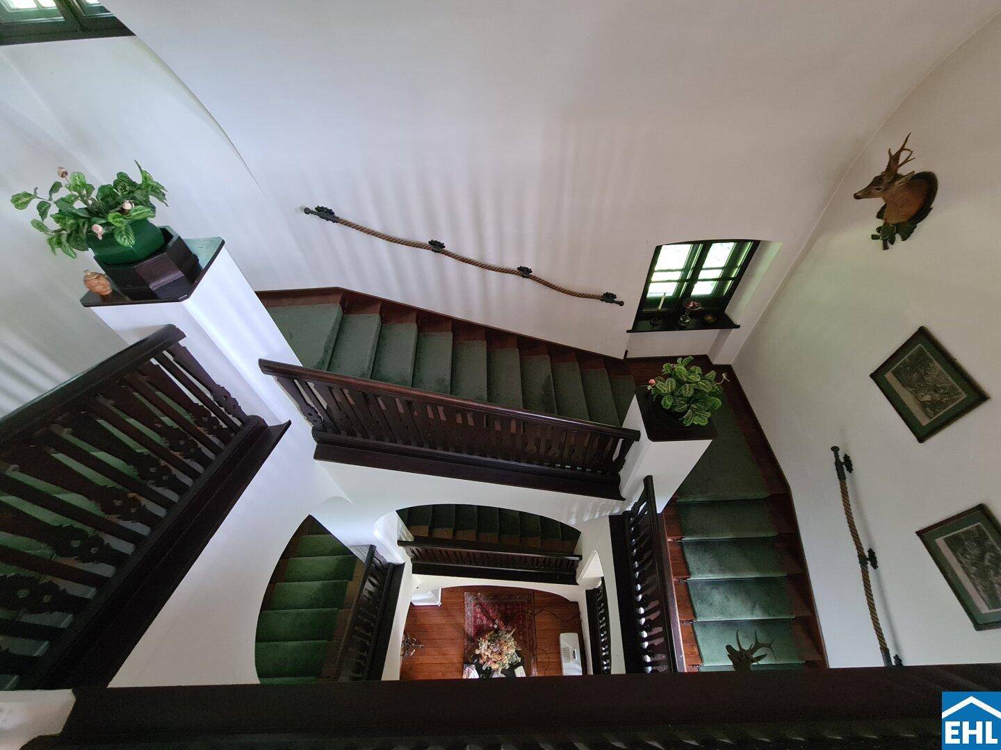 Elegantes Treppenhaus mit grünem Teppich, Holzgeländer und Jagdtrophäen an den Wänden.