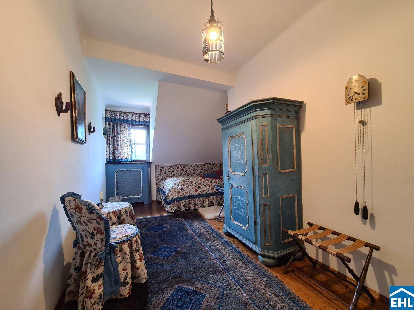 Kleines Schlafzimmer mit antikem Schrank, floralen Akzenten und Holzboden.
