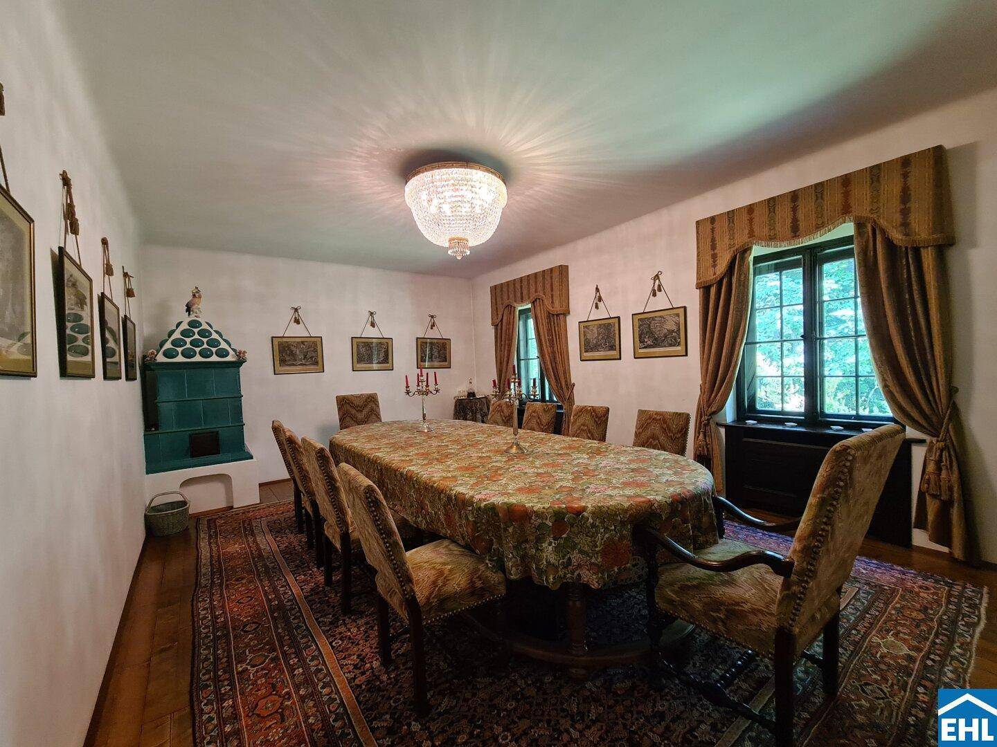 Klassisches Esszimmer mit großem Holztisch, Kachelofen und opulentem Kronleuchter.