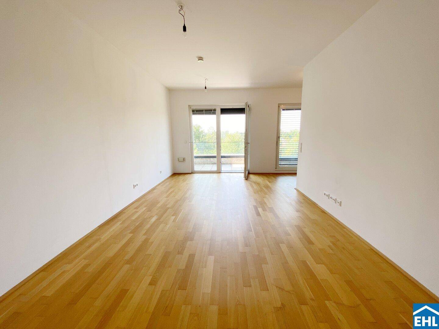 Geräumiges, helles Wohnzimmer mit Holzboden und großen Fenstern, die viel Licht hereinlassen.