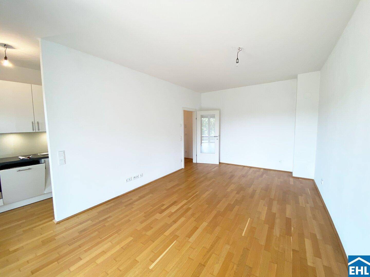 Offener Wohnbereich mit Parkettboden und teilweiser Sicht auf die angrenzende Küche.