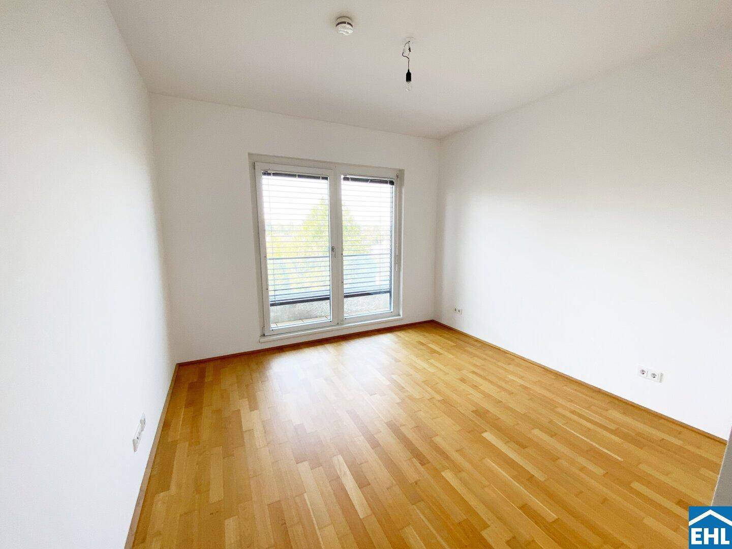 Helles Schlafzimmer mit Parkettboden und großem Fenster, das viel Tageslicht hereinlässt.