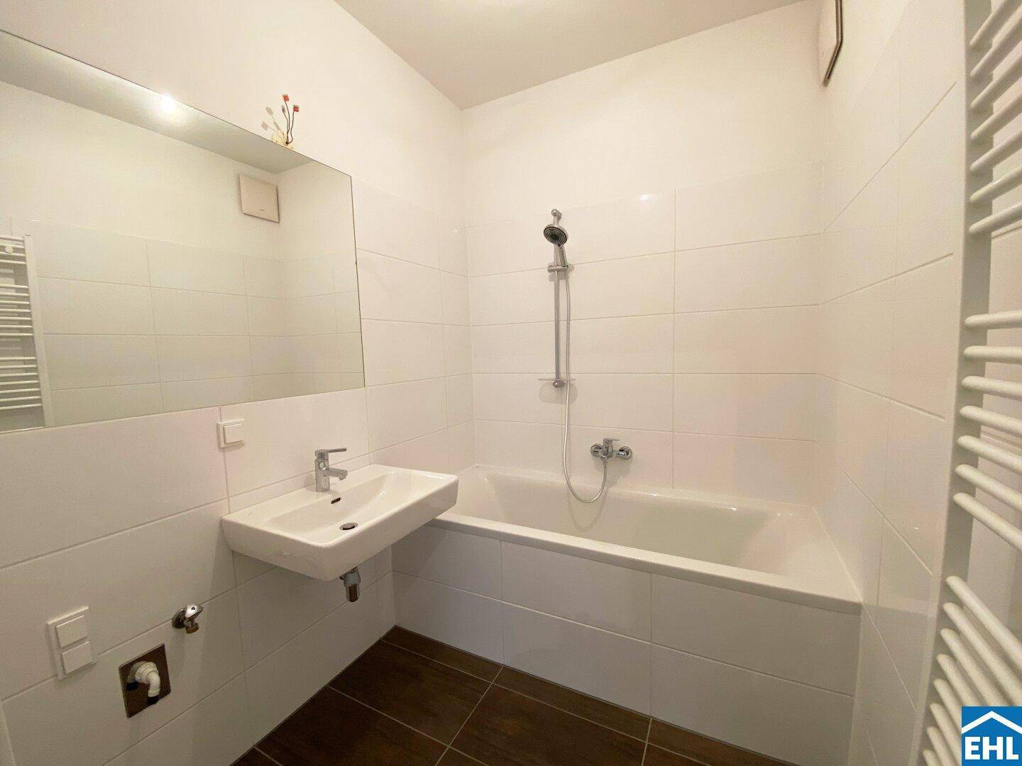 Modernes Badezimmer mit weißen Fliesen, Badewanne, Waschbecken und beheiztem Handtuchhalter.