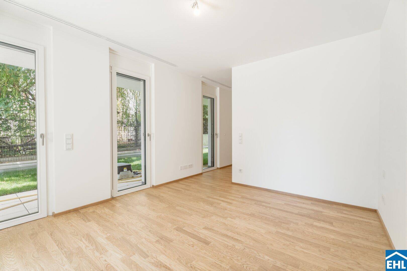 Heller Raum mit Parkettboden und großen Glastüren, die Zugang zum Garten bieten.