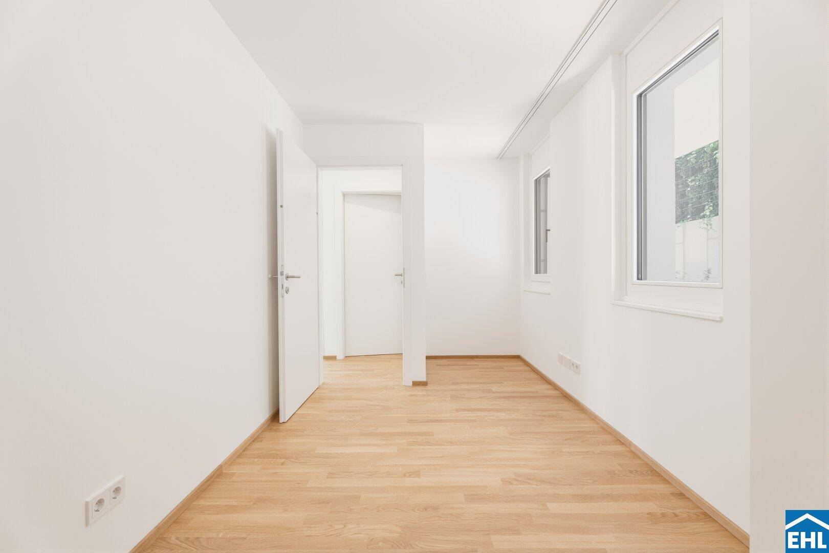 Helles Schlafzimmer mit Parkettboden und einem Fenster, das viel Tageslicht hereinlässt.