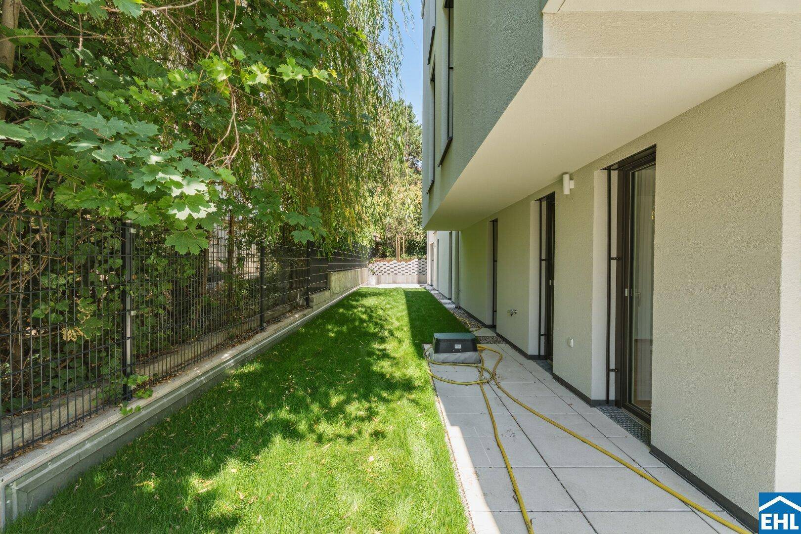 Langer, schmaler Gartenbereich mit gepflastertem Weg und üppiger Bepflanzung entlang der Fassade.