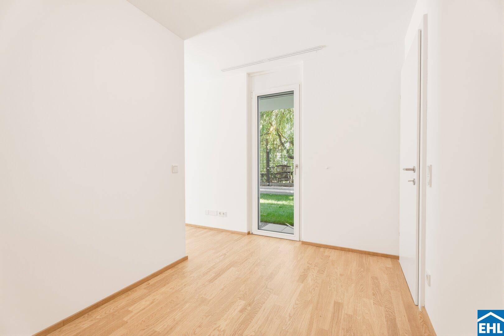 Leerer Raum mit Parkettboden und einer Glastür, die direkten Zugang zum Garten bietet.