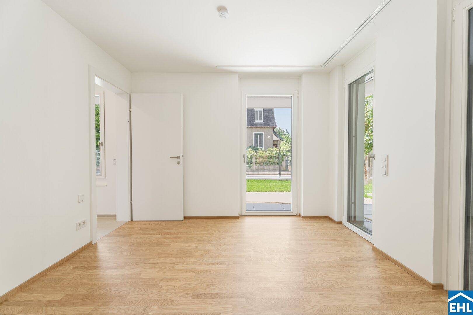 Geräumiger Raum mit Parkettboden und großen Fenstern, die viel Licht hereinlassen.
