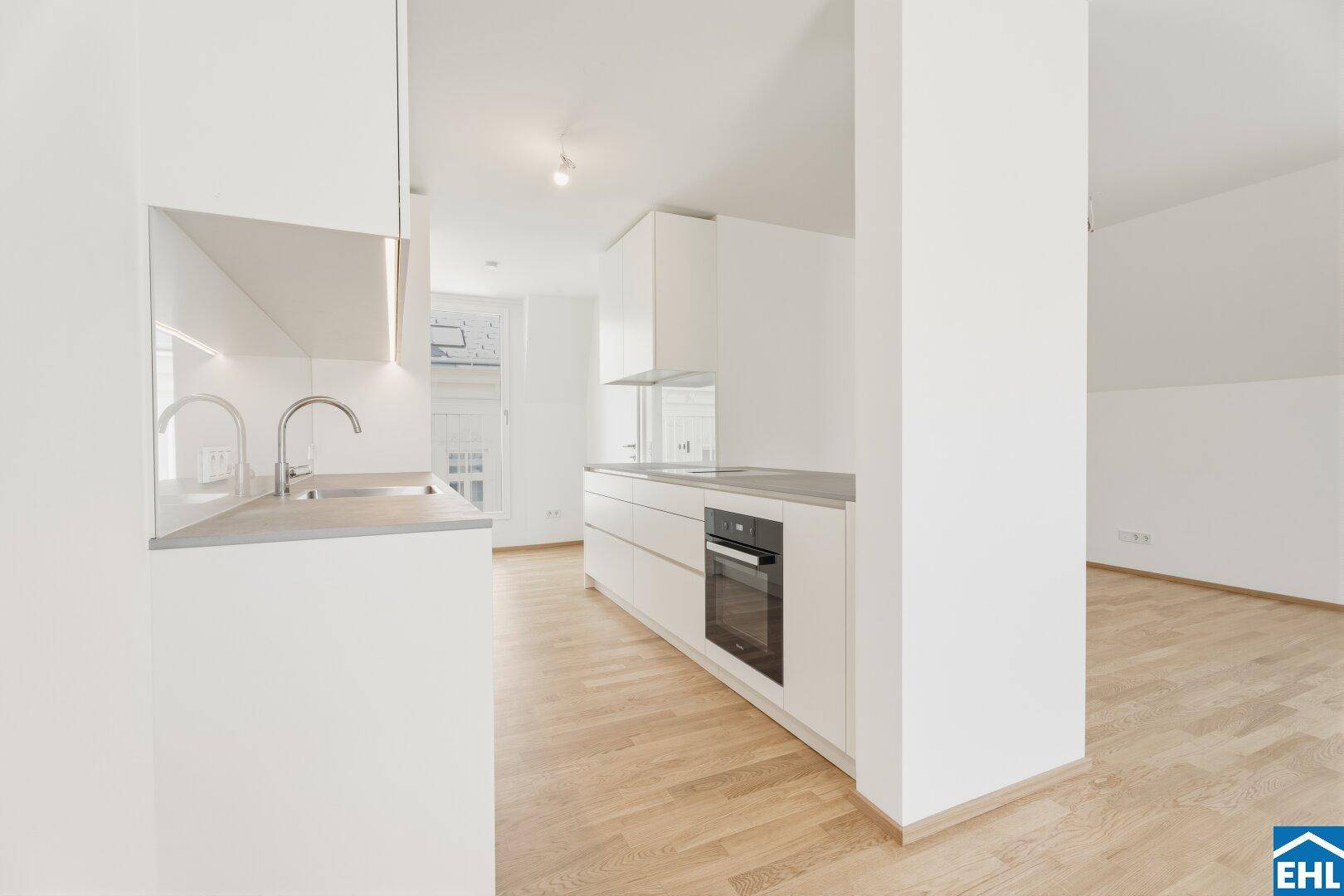 Moderne Einbauküche mit weißen Schränken, integriertem Backofen und grauer Arbeitsplatte.