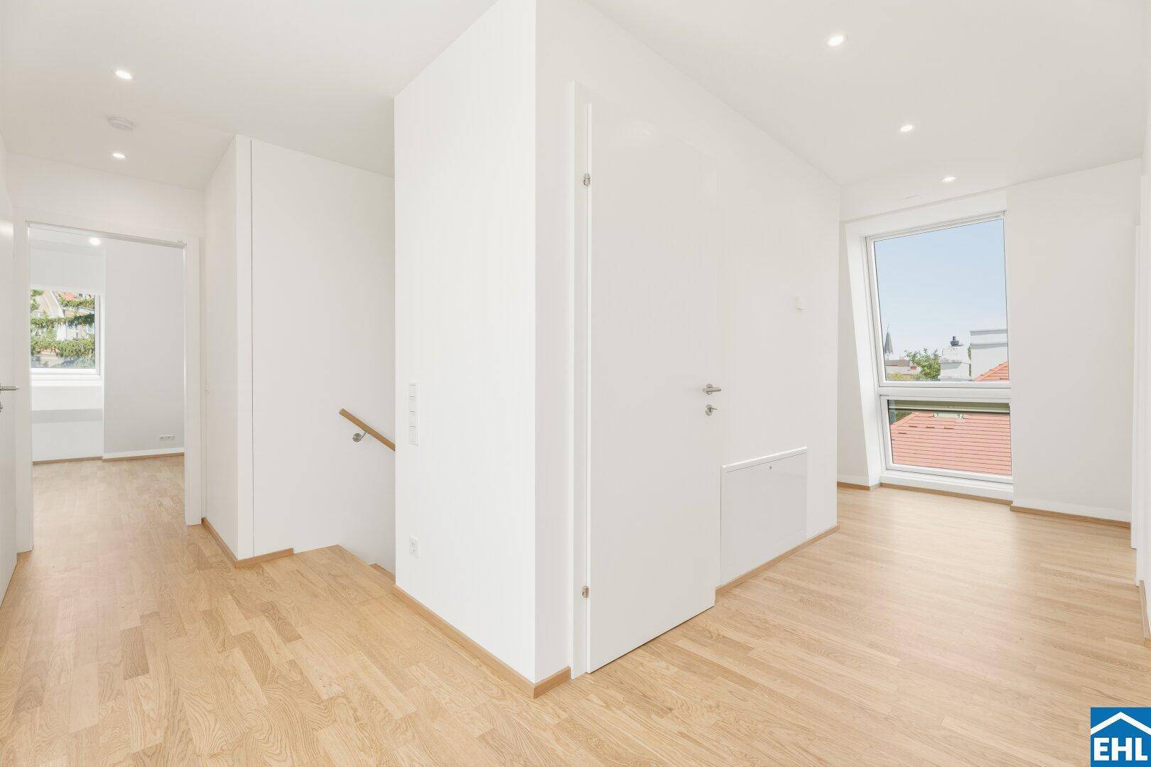 Heller Flur mit Holzboden, Einbaustrahlern und einem Fenster, das den Raum mit Licht erfüllt.