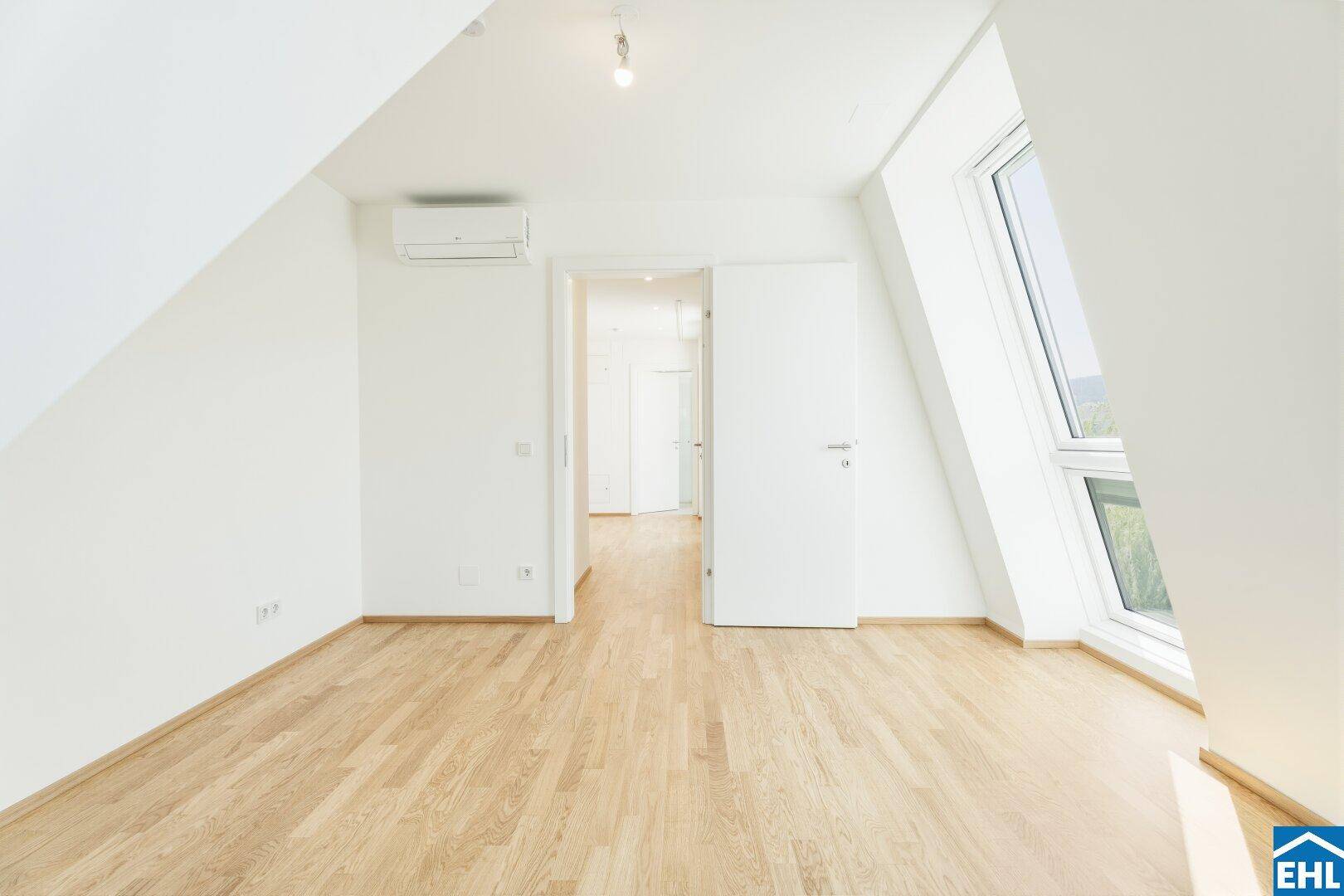 Geräumiger Raum im Dachgeschoss mit Holzboden, Klimaanlage und großem Fenster.