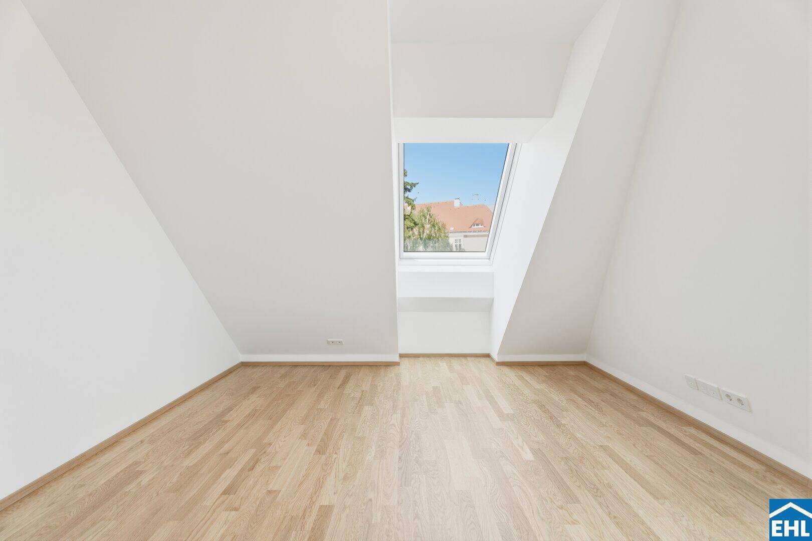 Heller Raum im Dachgeschoss mit Holzboden, schrägen Wänden und einem Dachfenster.