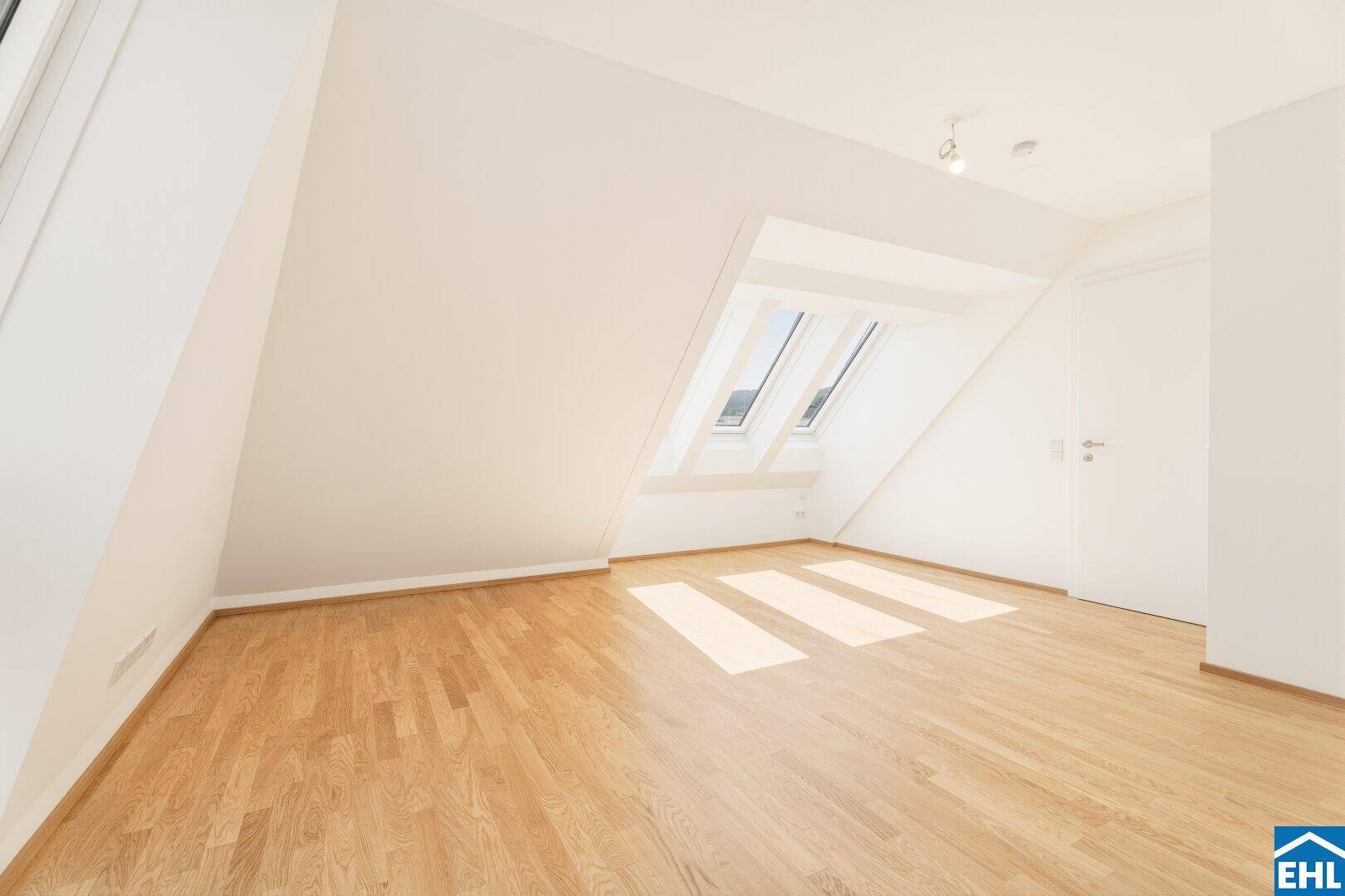 Lichtdurchfluteter Raum im Dachgeschoss mit Holzboden, schrägen Wänden und drei Dachfenstern.