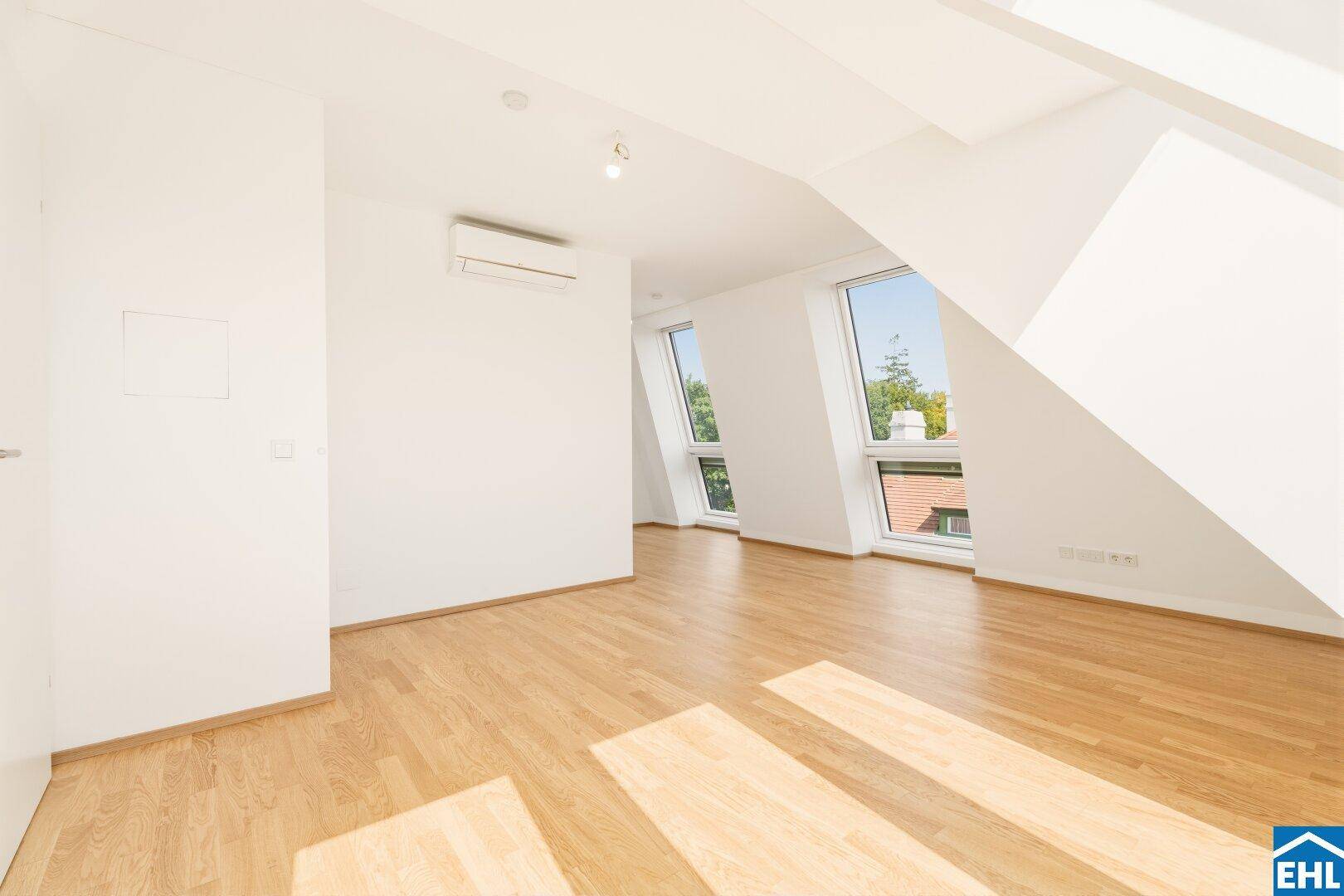 Heller Raum im Dachgeschoss mit Holzboden, Klimaanlage und großen Fenstern.