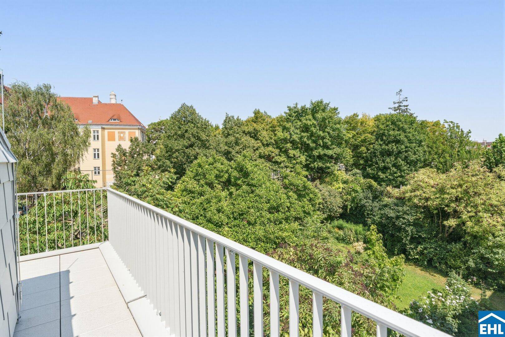 Geräumiger Balkon mit weißem Geländer und einem schönen Blick ins Grüne.