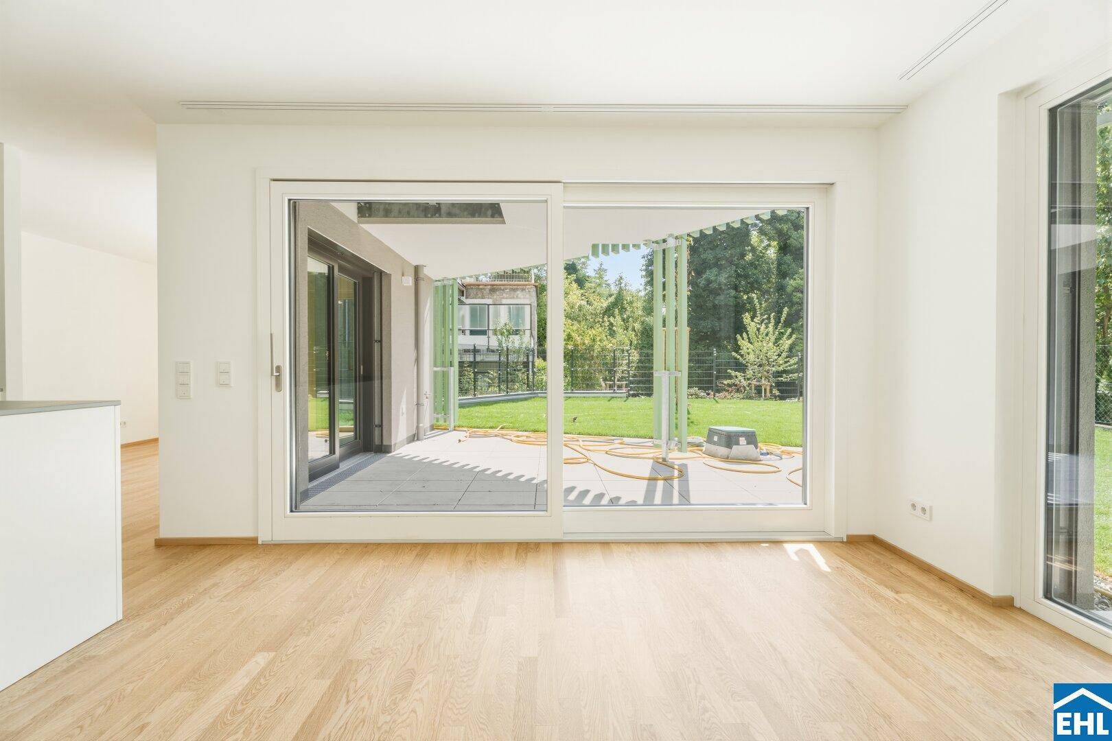 Geräumiges Zimmer mit Parkettboden und breiter Glasfront, die den Blick in den Garten freigibt.