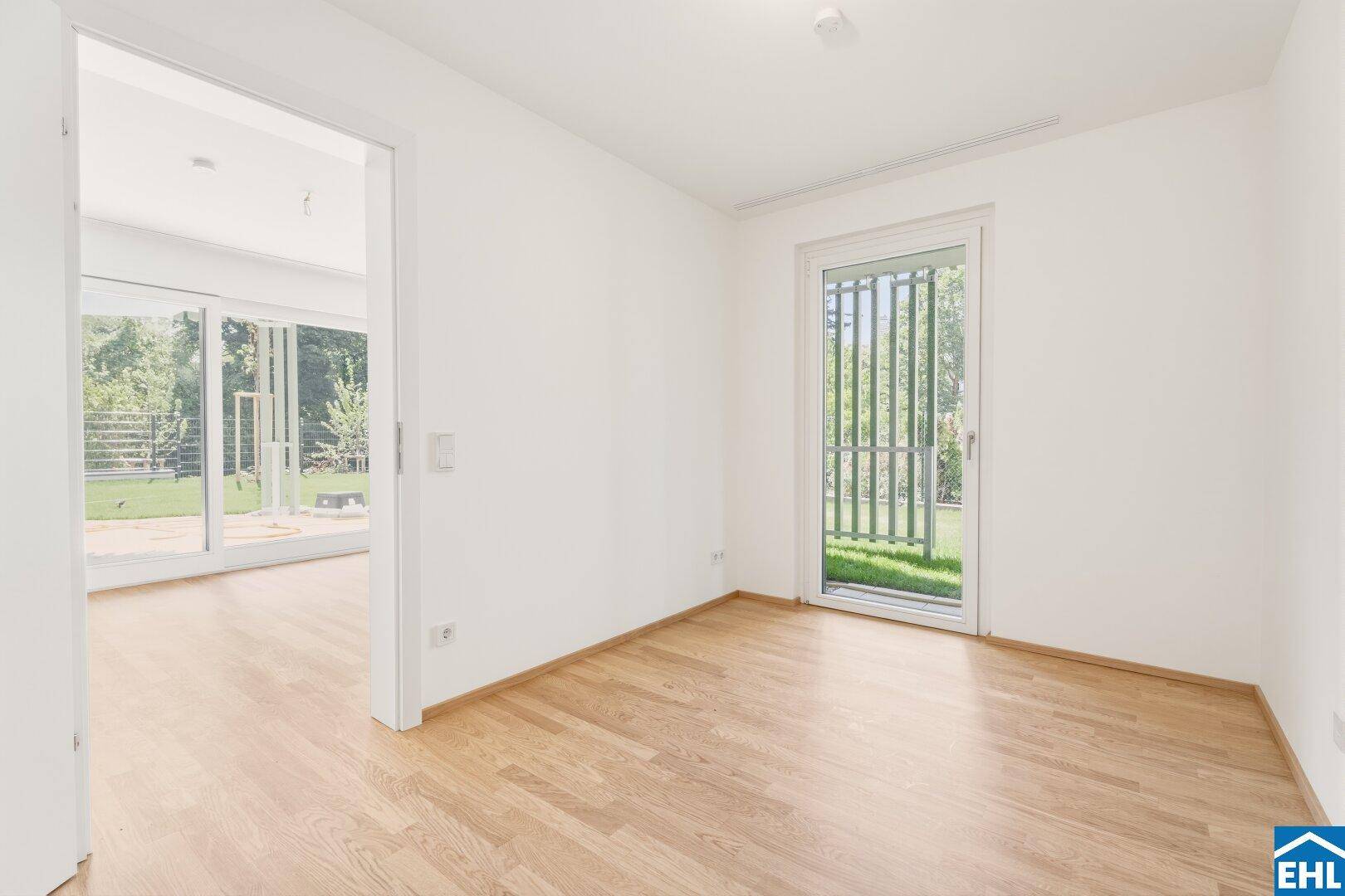 Helles Zimmer mit Parkettboden und Zugang zu einem kleinen Außenbereich oder Garten.
