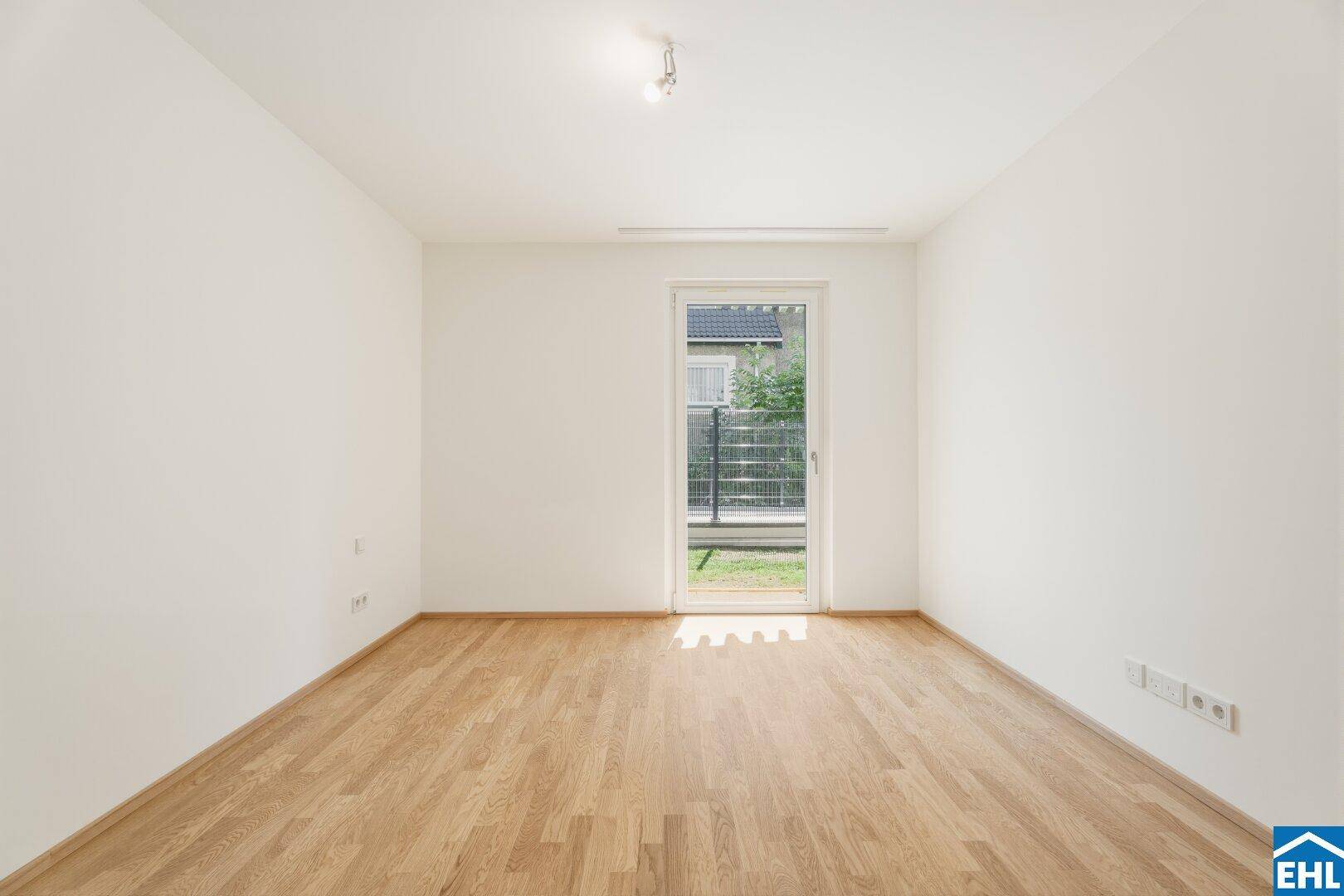 Unmöbliertes Zimmer mit Parkettboden und Zugang zu einem kleinen Außenbereich.