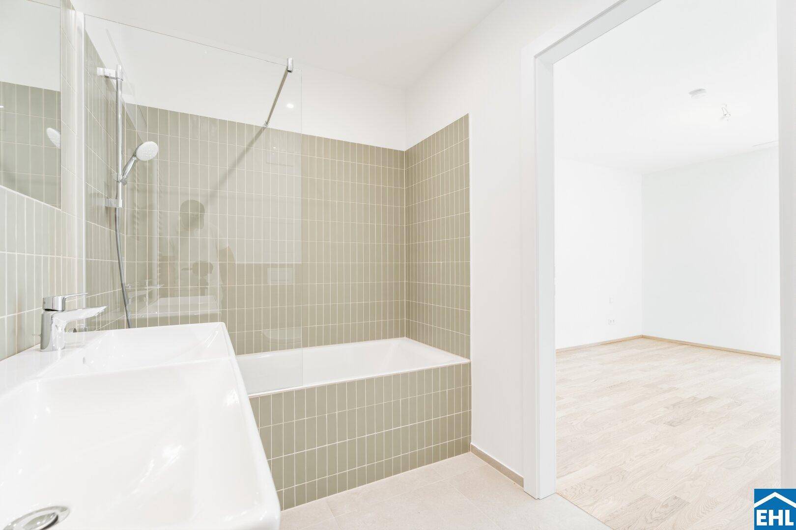 Helles Badezimmer mit Badewanne, Waschbecken und Zugang zu einem angrenzenden Zimmer.