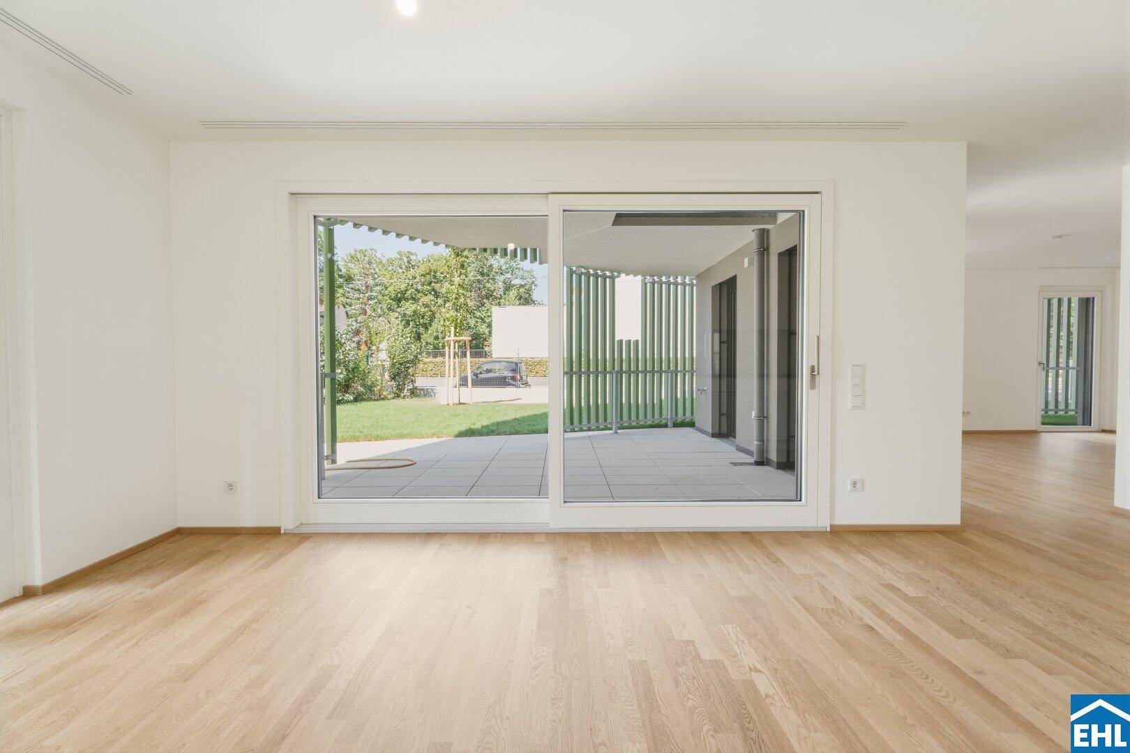 Geräumiges Wohnzimmer mit hellem Parkettboden und großen Schiebetüren zur Terrasse und zum Garten.