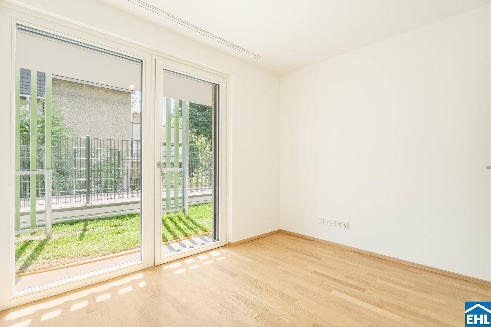 Lichtdurchflutetes Zimmer mit Parkettboden und Zugang zu einem kleinen Außenbereich.