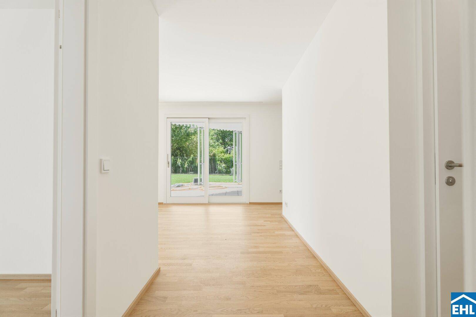 Heller Flur mit Holzboden, der zu einem lichtdurchfluteten Raum mit Gartenblick führt.