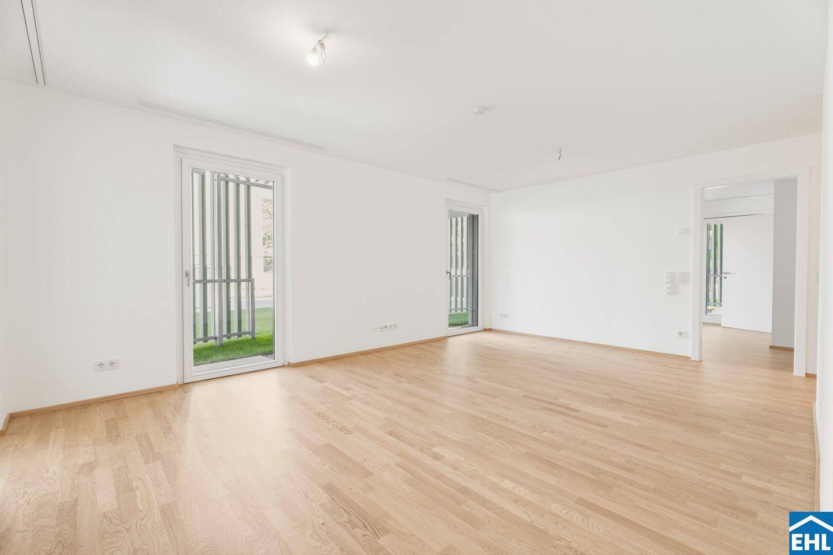 Heller Raum mit Parkettboden und zwei Türen, die Zugang zu einem Außenbereich bieten.