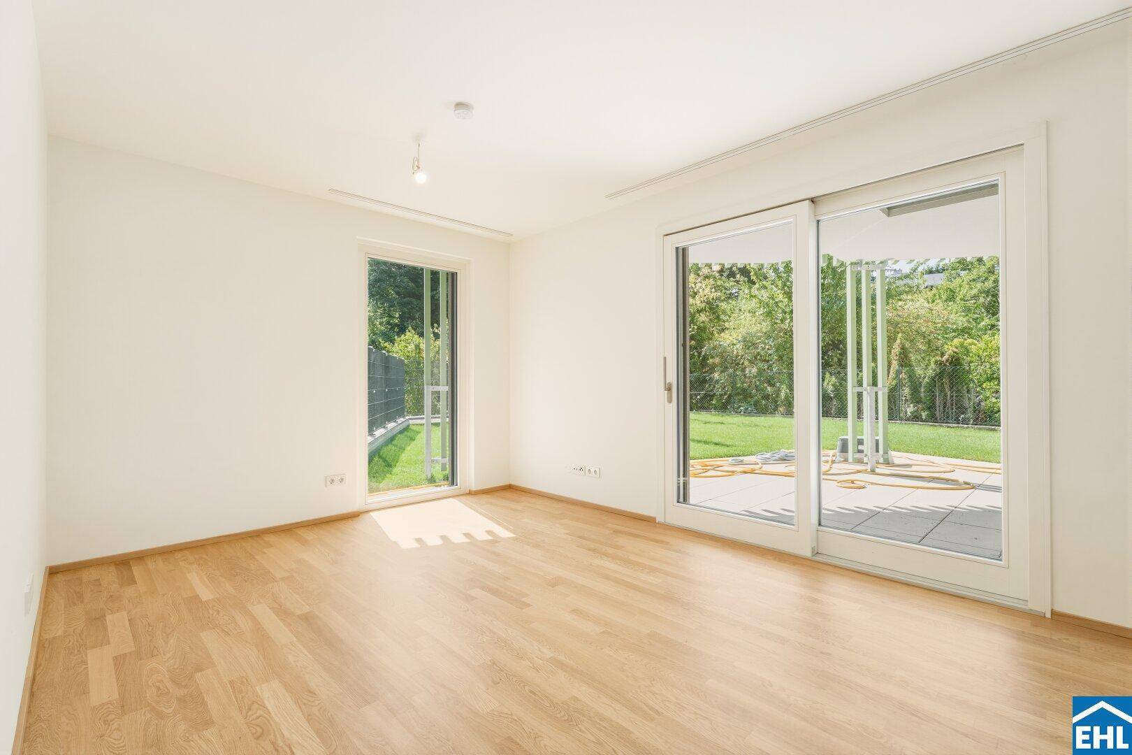 Geräumiges Zimmer mit Parkettboden und großen Fenstern, die viel Tageslicht hereinlassen.
