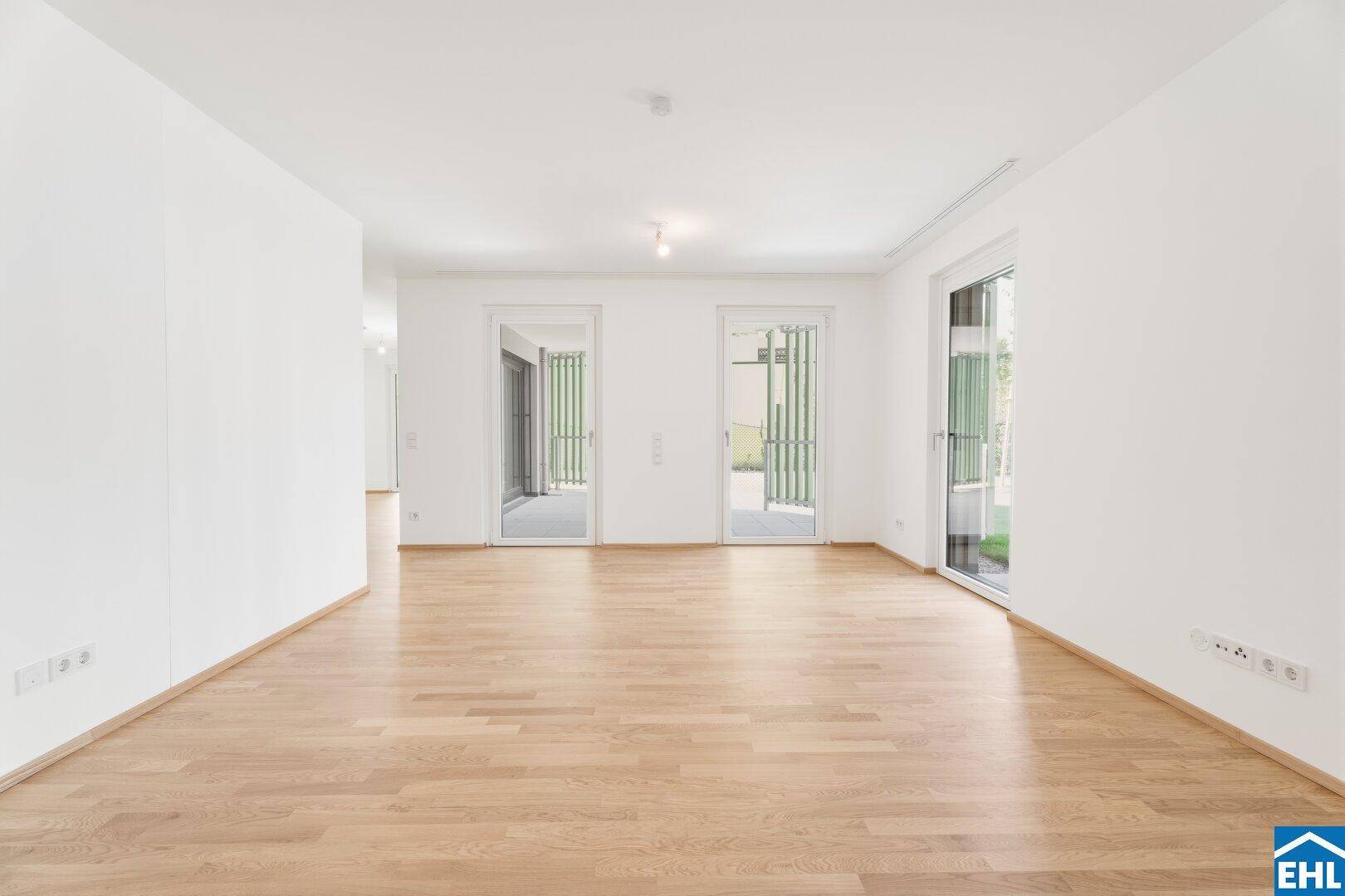 Geräumiger, heller Raum mit Parkettboden und mehreren Fenstertüren zum Außenbereich.