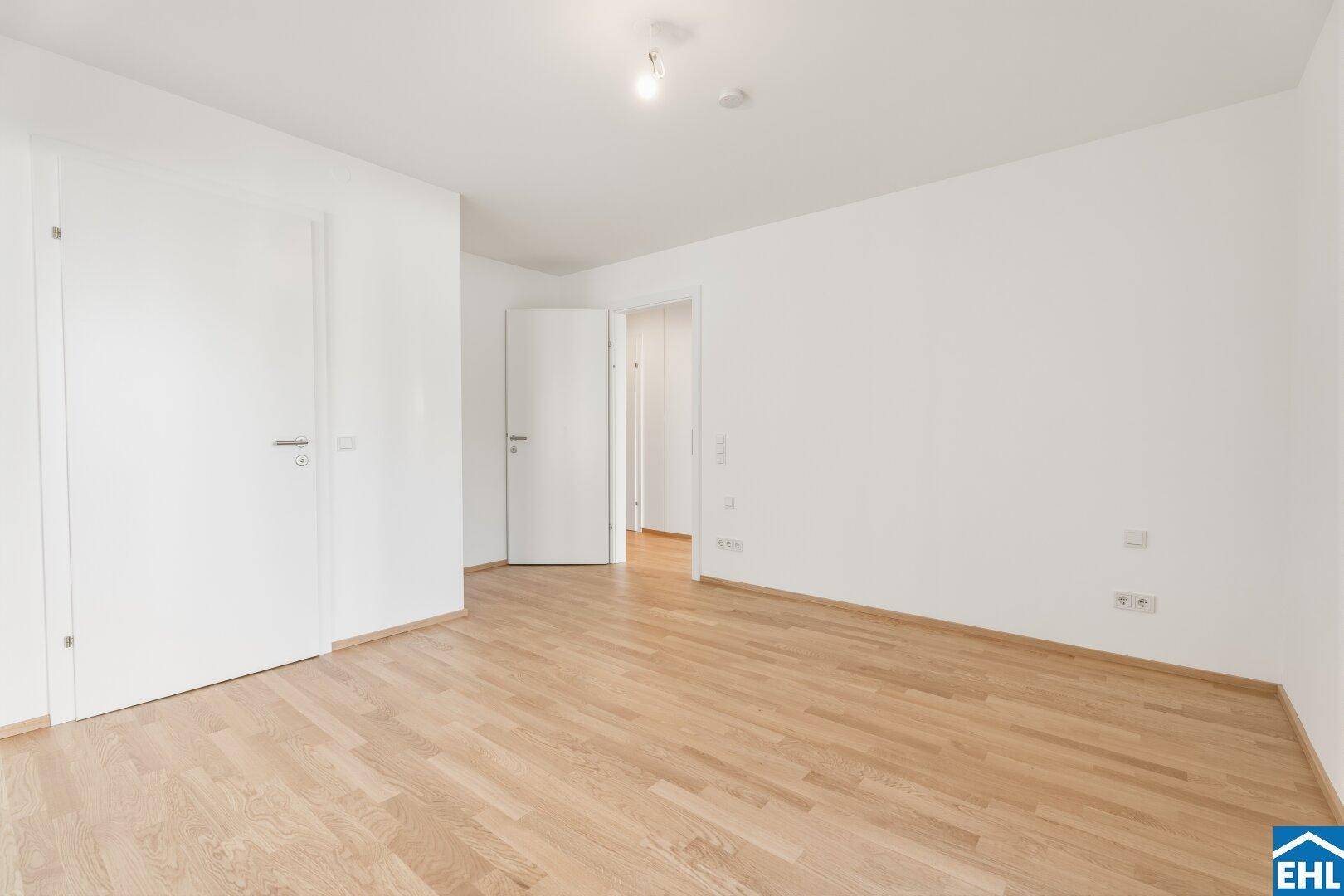 Helles Schlafzimmer mit Parkettboden und weiß gestrichenen Wänden, bereit zur individuellen Gestaltung.