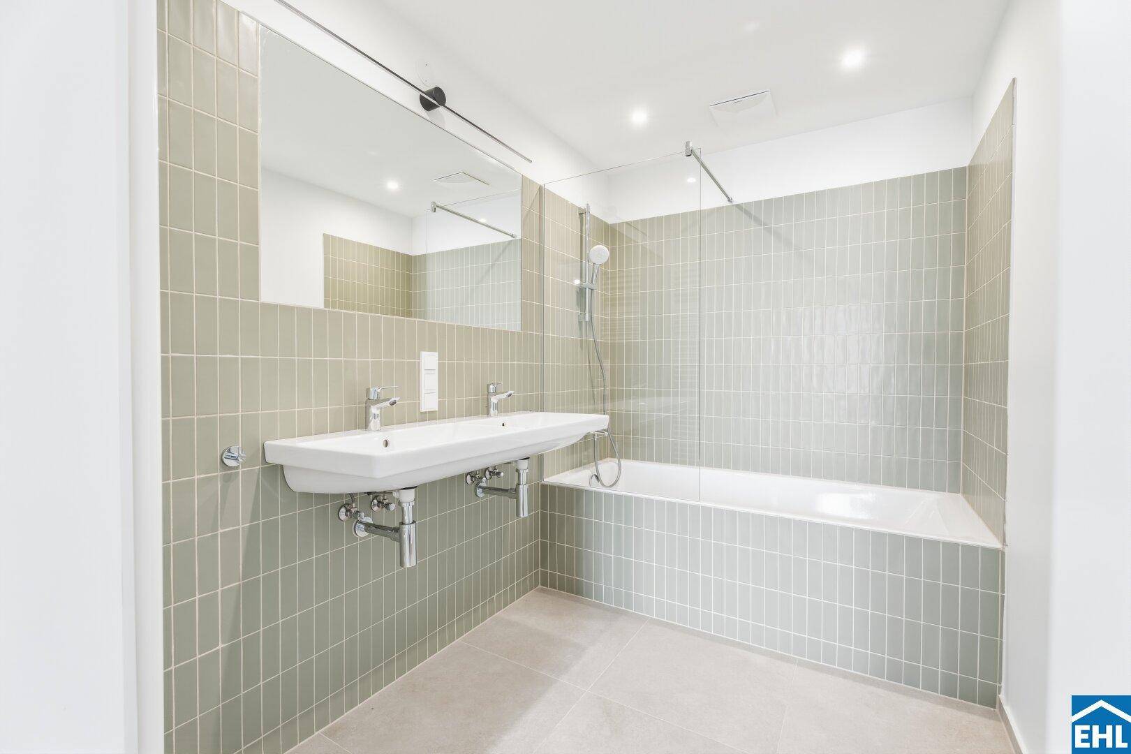 Modernes Badezimmer mit Doppelwaschbecken, Badewanne und eleganten hellgrünen Fliesen.