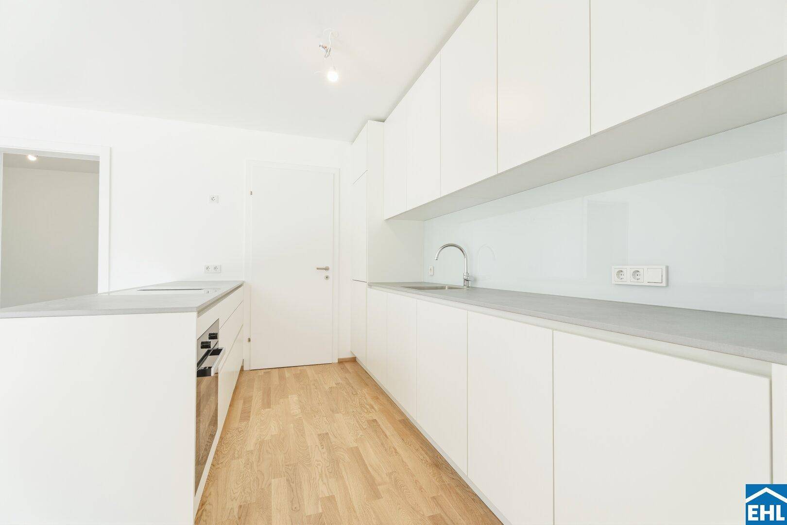 Moderne weiße Küche mit minimalistischen Schränken, integrierten Geräten und Holzboden.