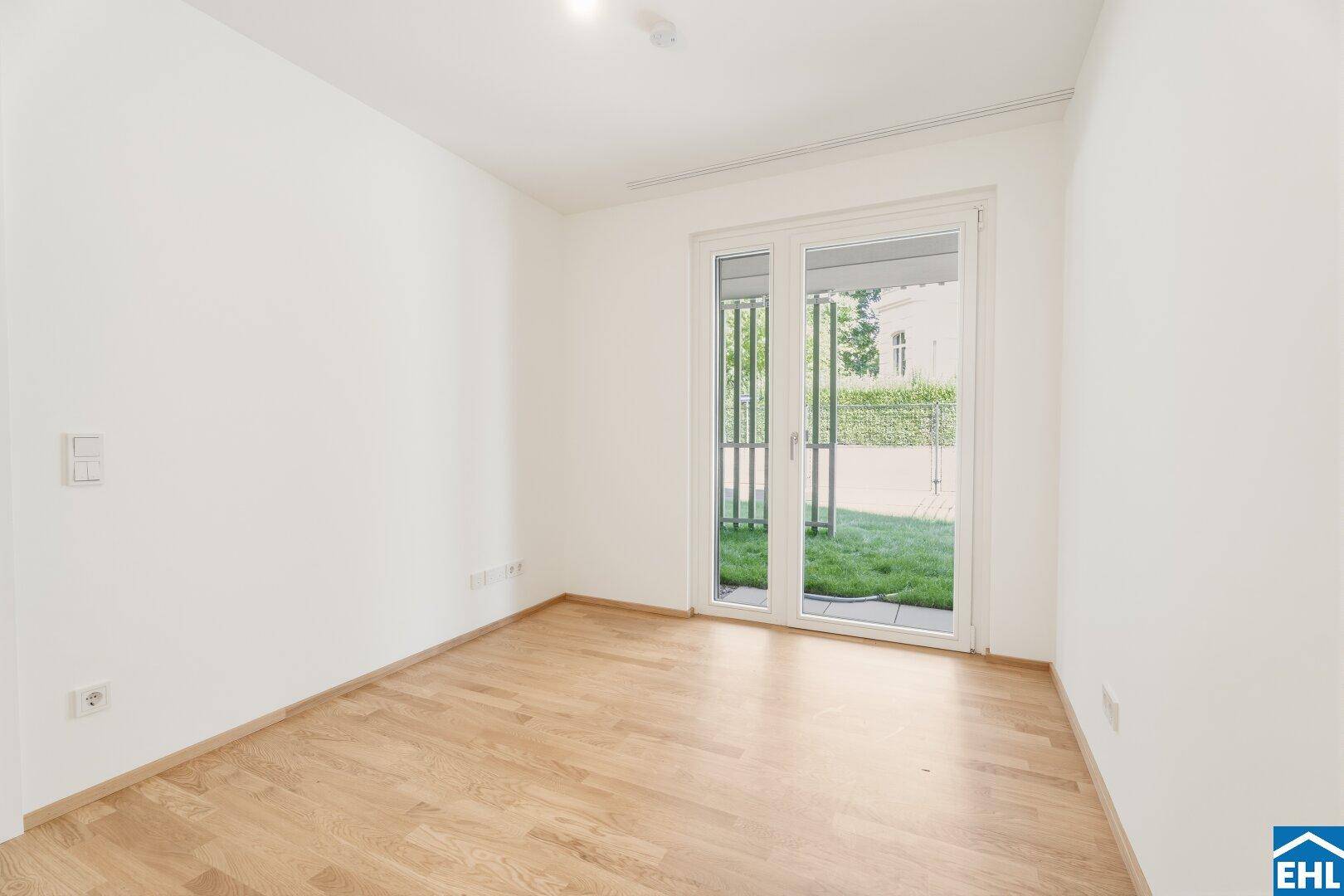 Helles Zimmer mit Parkettboden und direktem Zugang zu einem kleinen Gartenbereich.