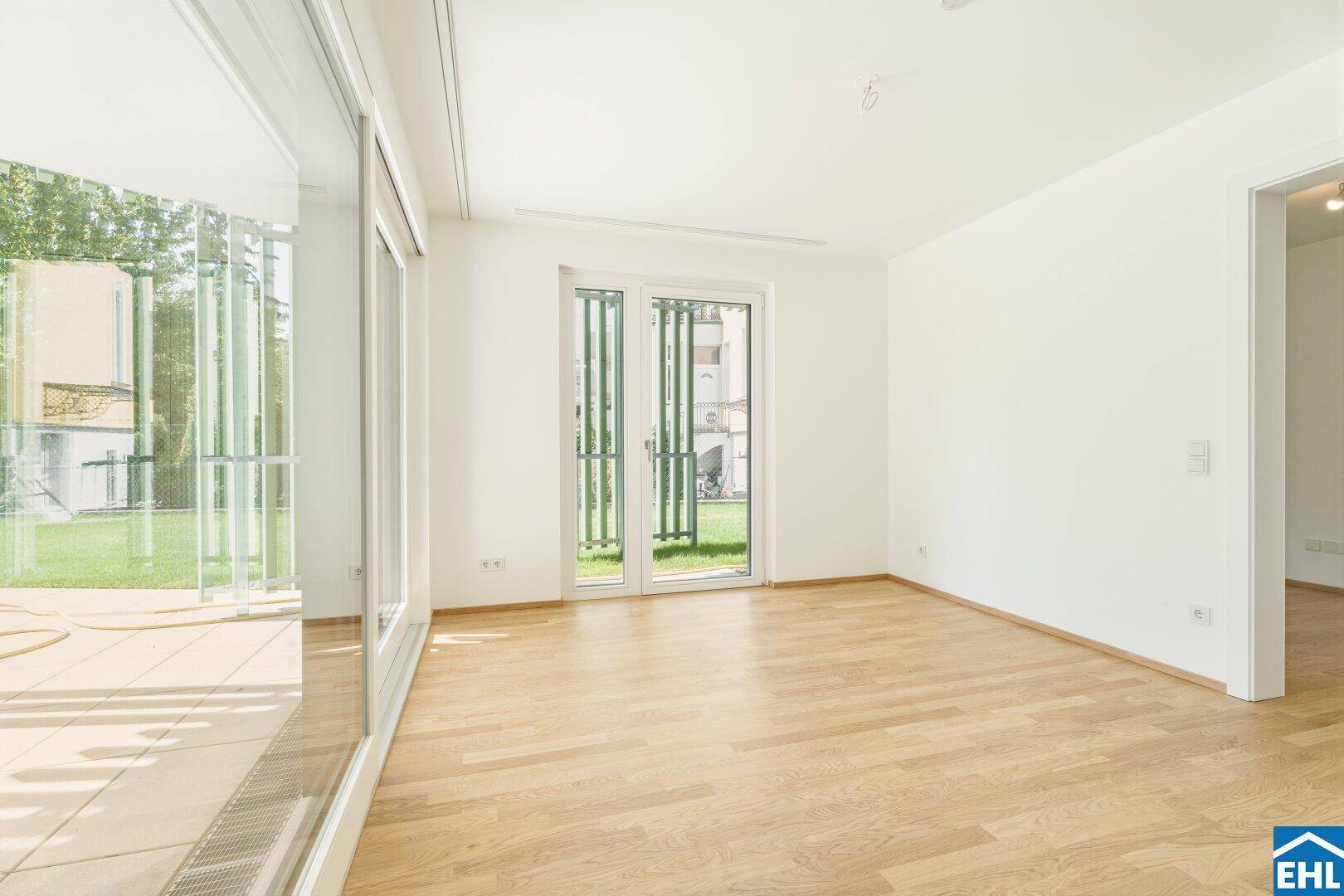 Lichtdurchflutetes Zimmer mit Parkettboden und großen Fenstern zum Garten und zur Terrasse.