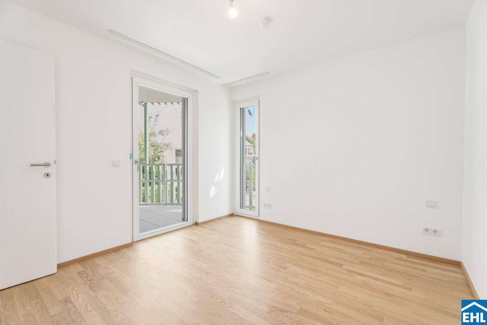 Helles Schlafzimmer mit Parkettboden und direktem Zugang zu einem sonnigen Balkon.